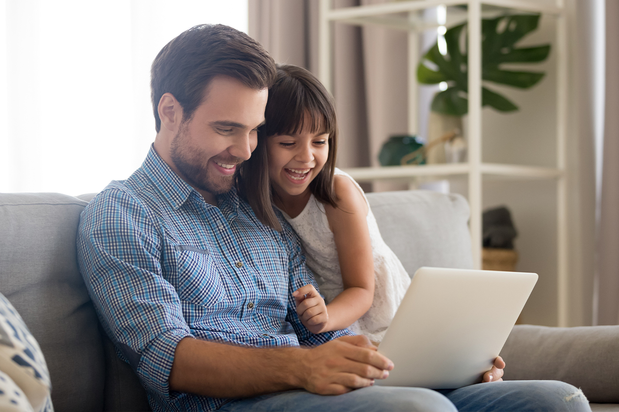 Young dad using laptop on the couch with his daughter