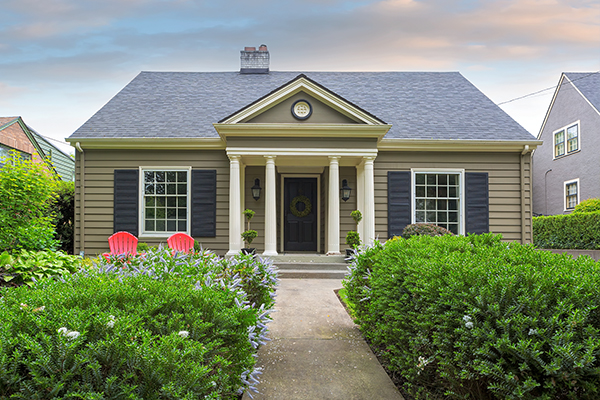 Small brown cottage with shrubbery in front yard