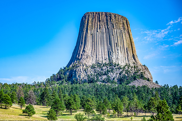 Devils tower in Wyoming with blue skies and green trees