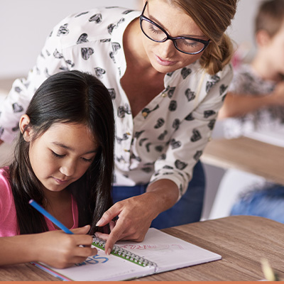 Young teacher helping child at desk