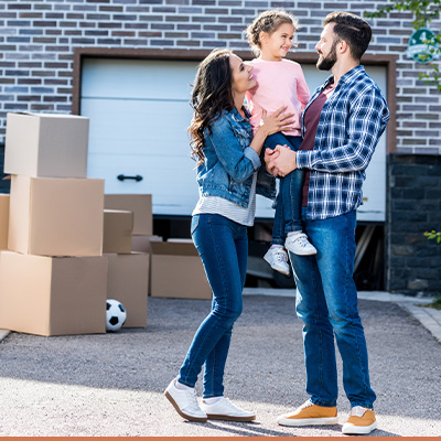 Young happy family in driveway with moving boxes around them