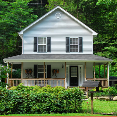 White farm house with green trees and shrubs in yard