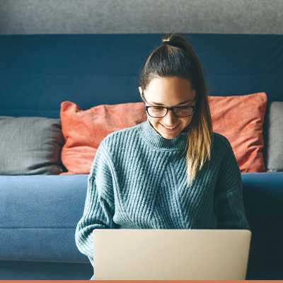 Young woman sitting on floor in front of sofa on her laptop