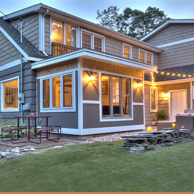 Patio area of tan two story home with string lights and white window trim